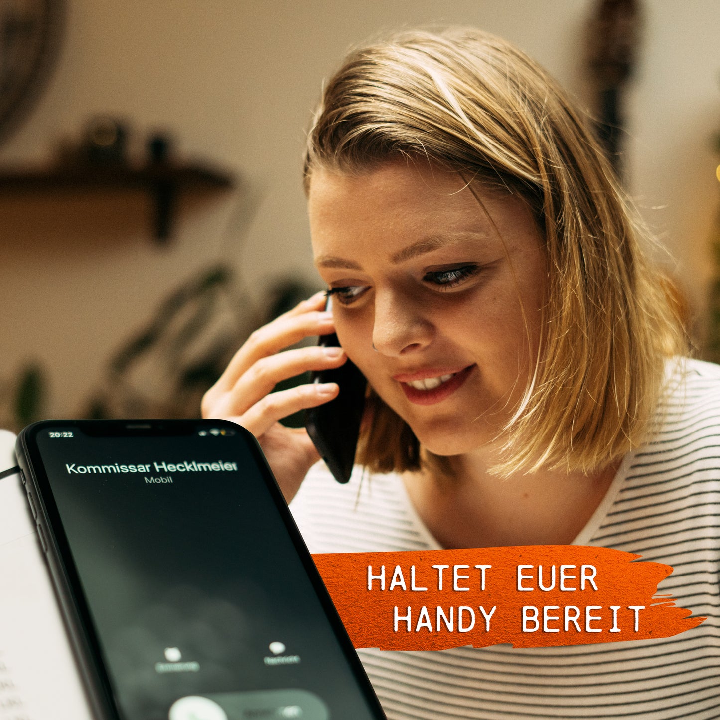 Eine Frau mit schulterlangem Haar spricht auf ihrem Smartphone. Auf einem anderen Telefon wird ein eingehender Anruf von „Kommissar Heddemer“ mit dem Text „HALTET EUER HANDY BEREIT“ angezeigt, der die Spannung von Krimispiel: Tatort Kunstfehler einfängt.