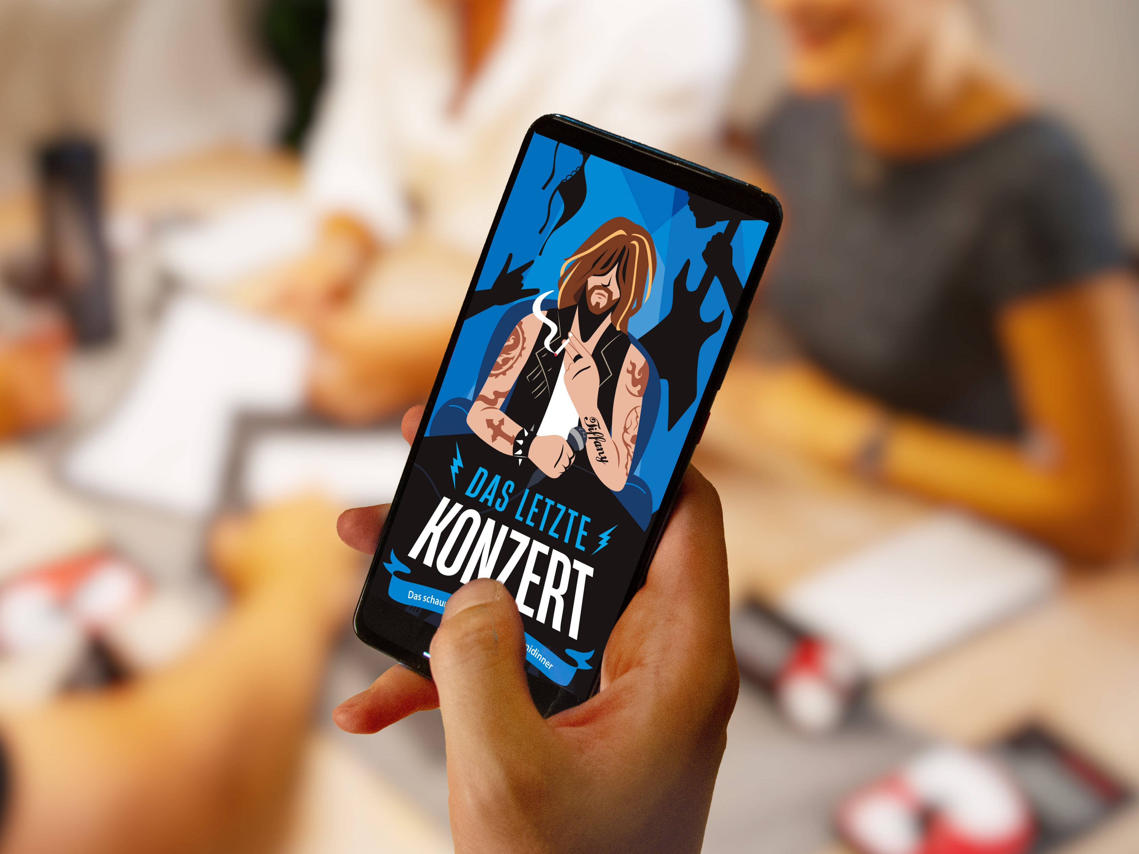 Eine Person hält ein Smartphone, auf dem die Illustration eines Rockmusikers mit langen Haaren und Tattoos zu sehen ist. Der Text lautet „Das letzte Konzert“. Im Hintergrund sind Menschen in einer Besprechungssituation zu sehen, auf dem Tisch liegen Papiere und Stifte.
