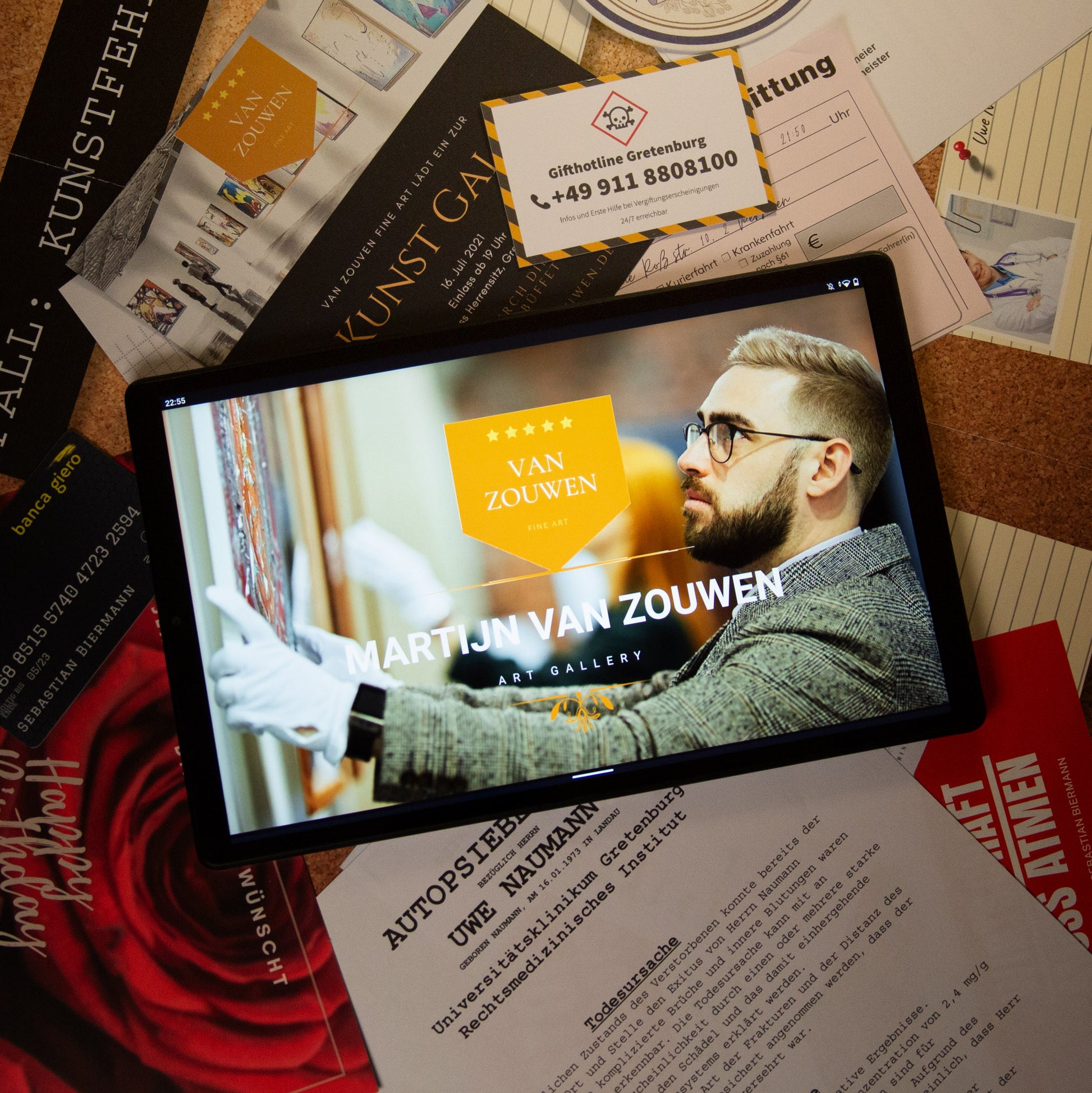 Ein Tablet mit der Website der Kunstgalerie „Martijn Van Zouwen“ liegt auf einer unordentlichen Pinnwand. Umgeben von Visitenkarten, Flyern und Papieren in deutscher und englischer Sprache. Zwei behandschuhte Hände sind zu sehen, die Kunstwerke auf dem Tablet-Bildschirm anfassen.